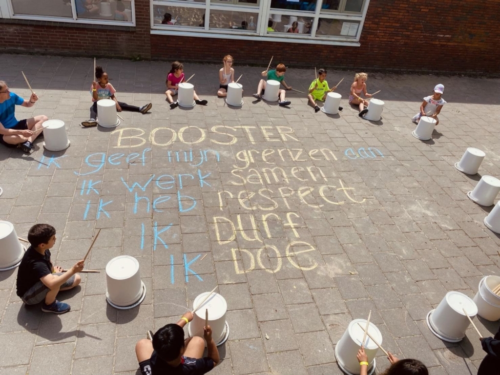 Kinderen trommelen rond de Boosters-regels in stoepkrijt